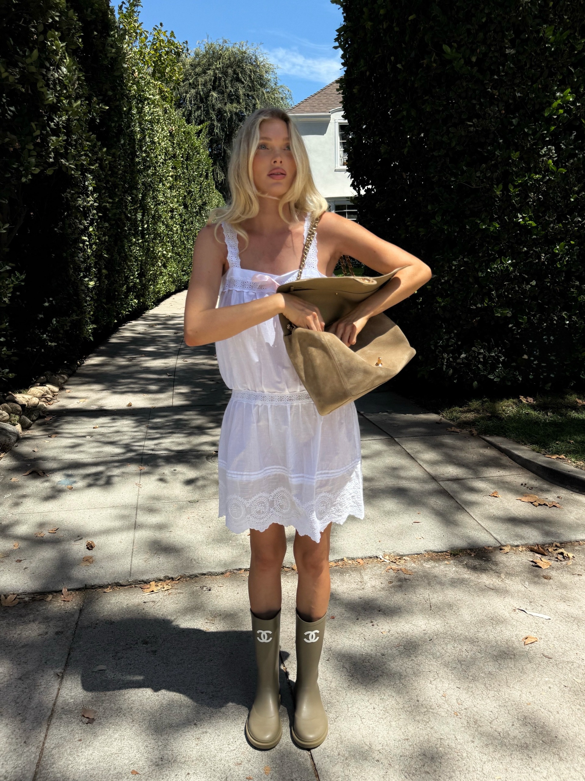 Elsa Hosk wearing a white dress, Chanel boots, and a beige suede Chanel Maxi Flap Bag.