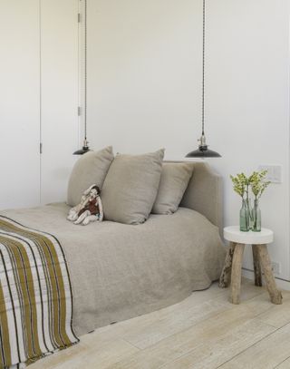 A bed with neutral brown bed sheets under pendant lighting
