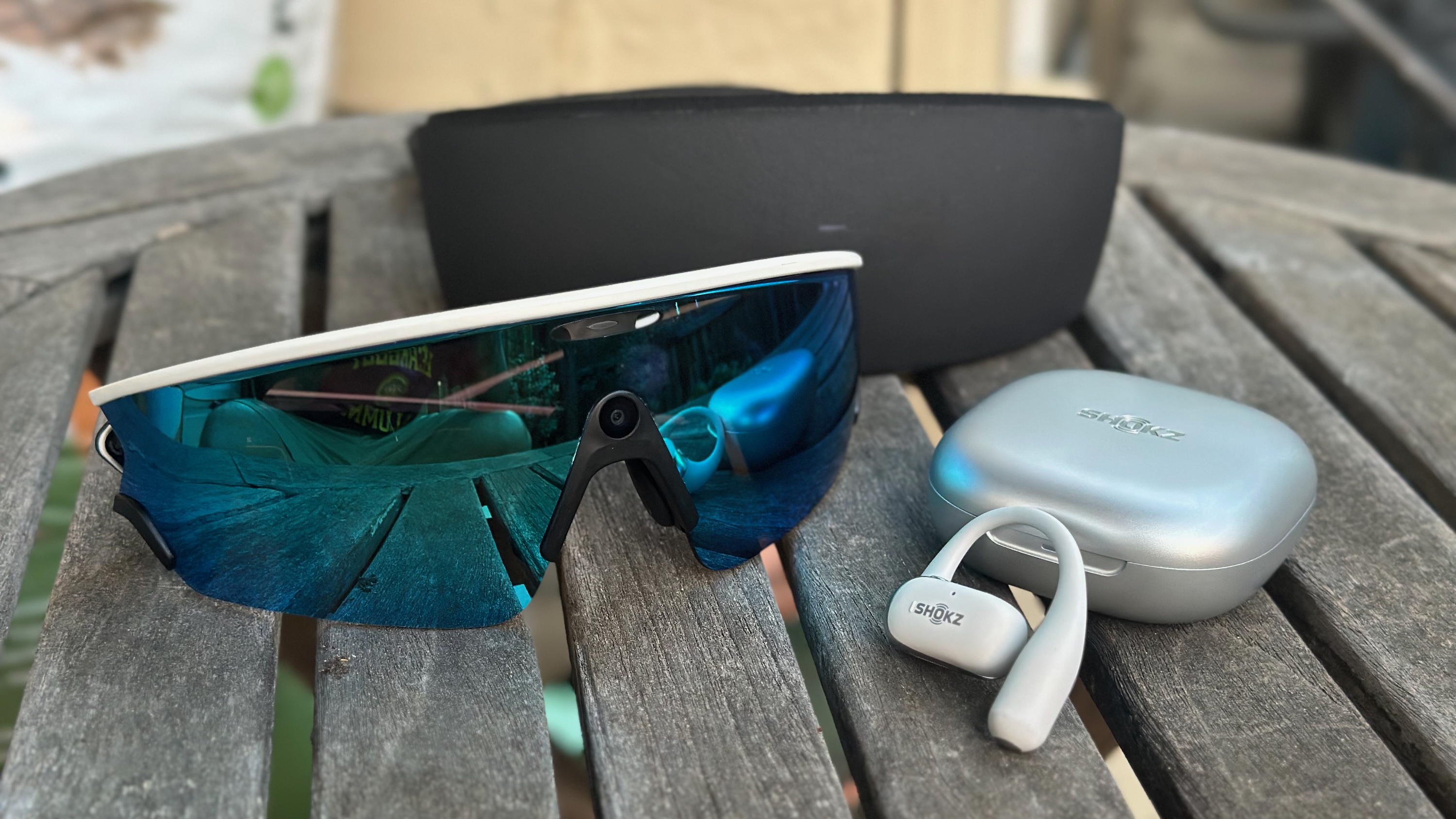 A photo of the Oakley Meta Vanguard glasses and Shokz OpenFit 2+ earbuds sitting on a table.
