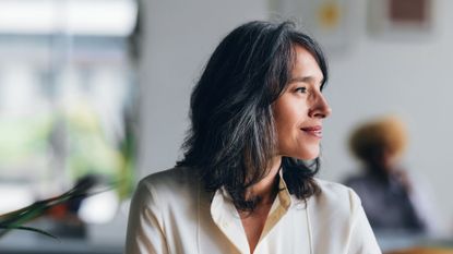 Woman with menopause symptoms smiling away from the camera in office wearing shirt