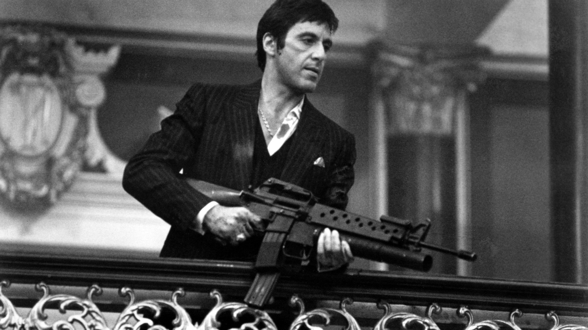 Al Pacino in Scarface standing on a balcony holding a gun 