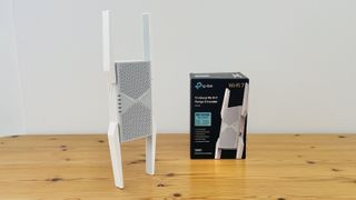 TP-Link BE10000 Wi-Fi range extender on wooden desk