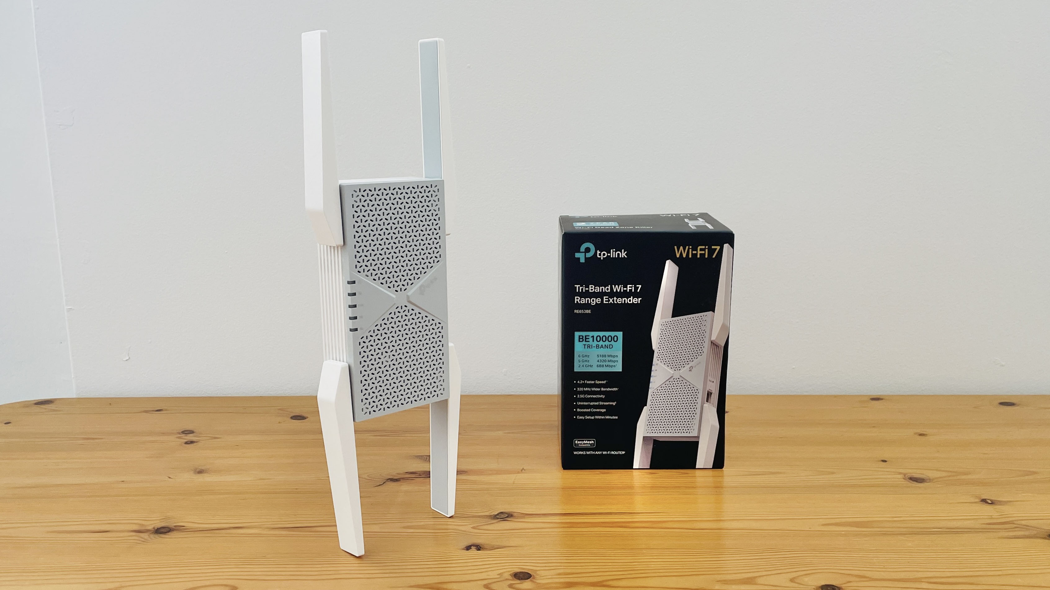 TP-Link BE10000 Wi-Fi range extender on wooden desk