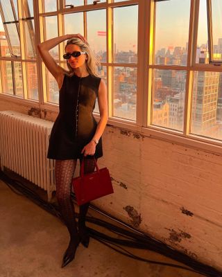 Eliza Huber wearing a black sculpted Tory Burch minidress with patterned tights, a red bag, and black kitten heel pumps.
