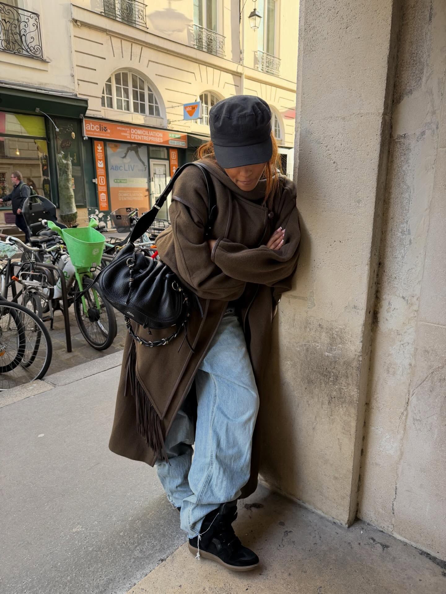 Fashion person @mv.tiangue wears a Gen Z spring outfit idea. She wears a brown wool scarf coat, baggy jeans Beckett wedge trainer and a baker boy hat. This image was taken from her Instagram recently.