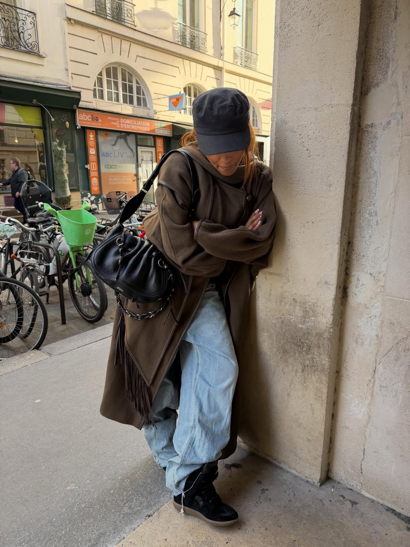 Fashion person @mv.tiangue wears a Gen Z spring outfit idea. She wears a brown wool scarf coat, baggy jeans Beckett wedge trainer and a baker boy hat. This image was taken from her Instagram recently.