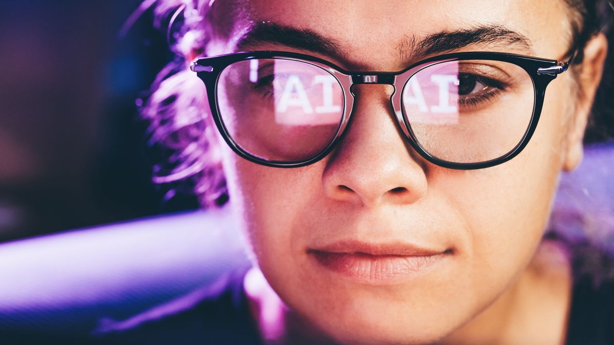 A close up of a woman working at a computer, with the letters AI reflected in her glasses