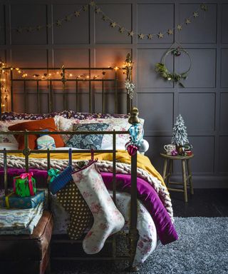 A dark grey bedroom with wall paneling and assortment of layered colorful throws and patterned bedding on bed