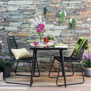 outdoor dining area with stone wall and bistro set and wooden floor