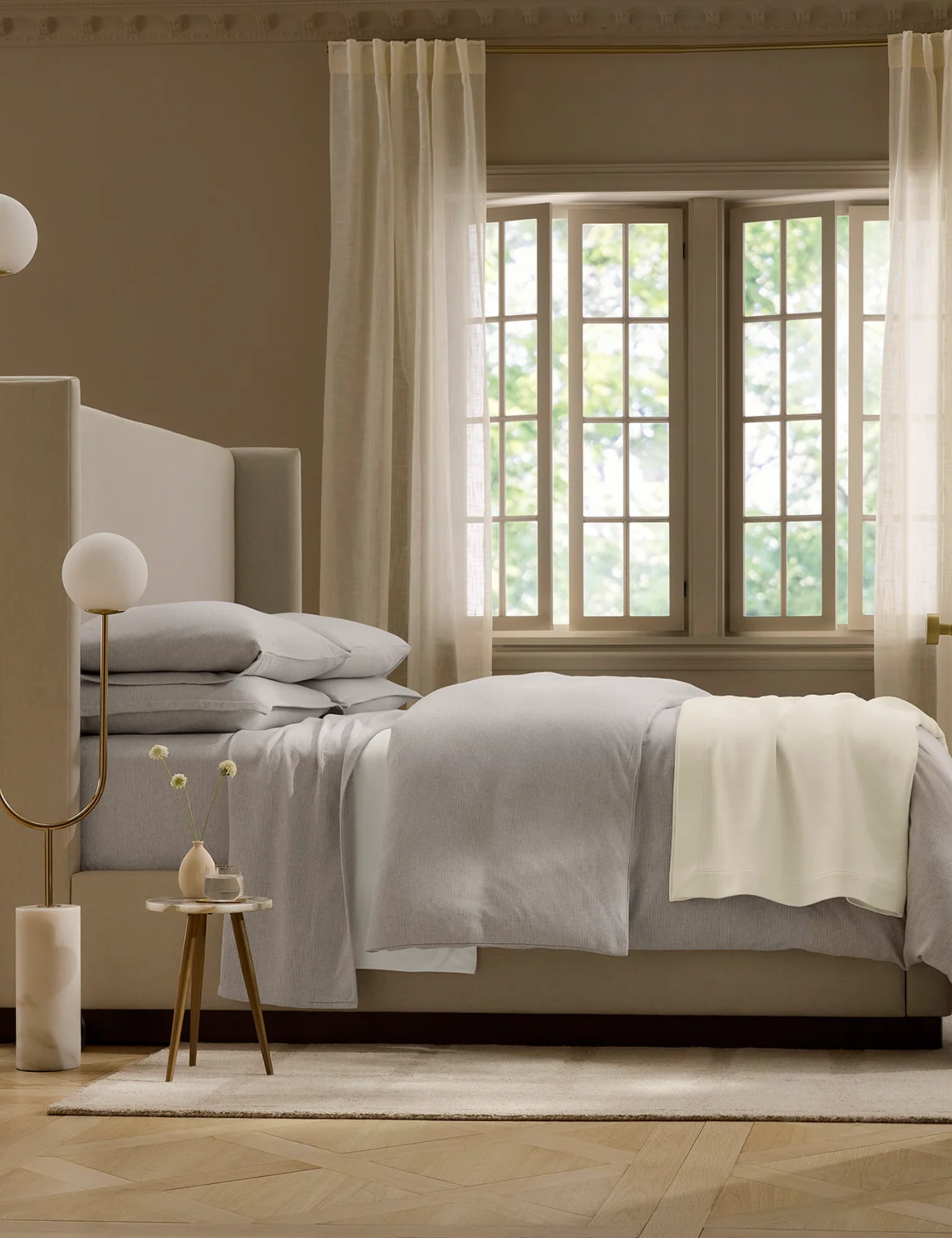 Grey flannel bed sheets pictured in a minimalist bedroom that features large windowpanes