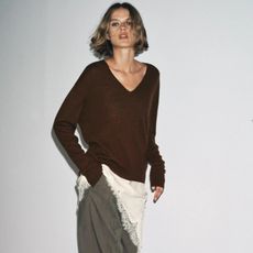 a product model shot from Zara of model wearing a brown v-neck sweater layered over a cream lace-hem silk dress and gray pants