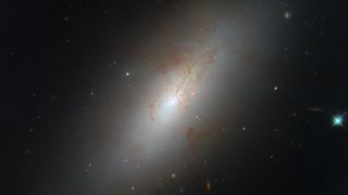 An image of NGC 4694, a smooth, glowing galaxy shaped like an ellipse with barely any star formation