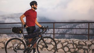 A man with a beard stands astride a triban bike with bikepacking bags