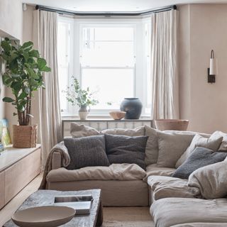 A neutral-coloured living room with a soft sofa and pleated curtains