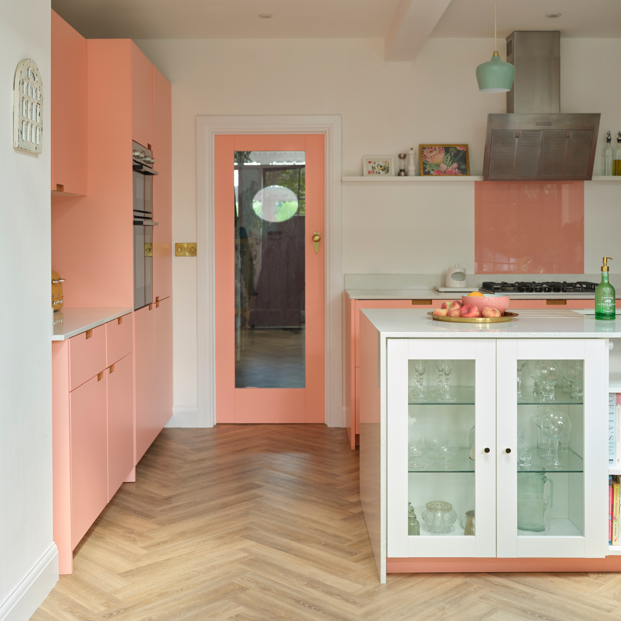 pink kitchen cabinets with a white kitchen island, matching pink framed glass door and herringbone wood flooring