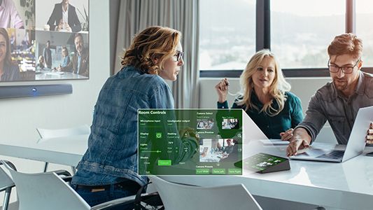 Three business people sit around a computer in a boardroom using Q-SYS solutions.