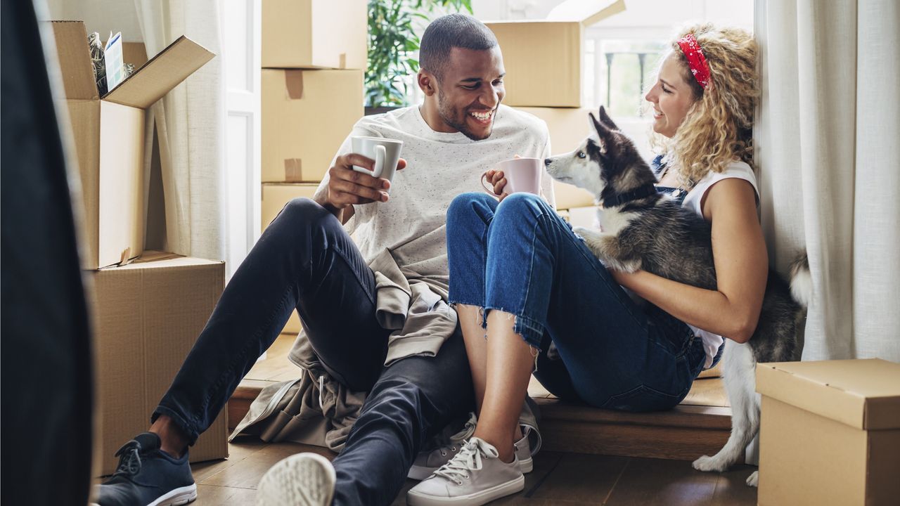 A happy couple sits among moving boxes in their new home.