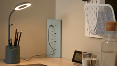 IKEA SKOTAT Extension cord, in green, on a desk next to a lit desk light