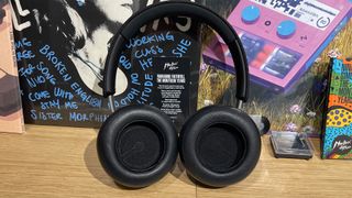 Dali IO-8 wireless over-ear headphones on wooden shelf with busy background with inside of earcups toward camera