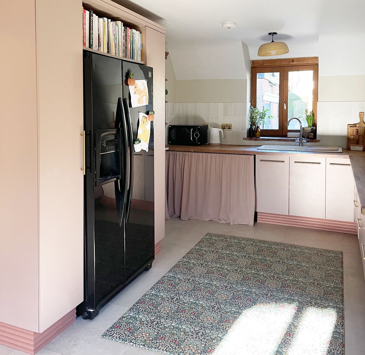 A pink kitchen with a black fridge with a built in shelving surround 