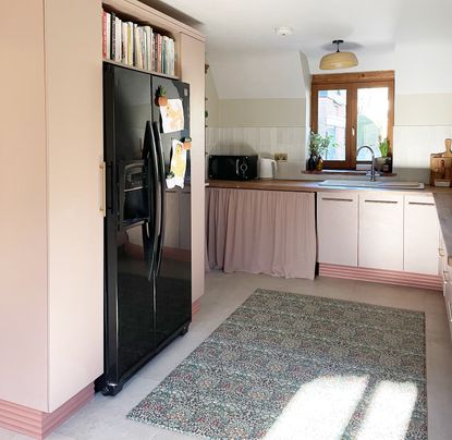 A pink kitchen with a black fridge with a built in shelving surround 