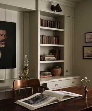 A neutral office with a large portrait painting and built-in bookshelves