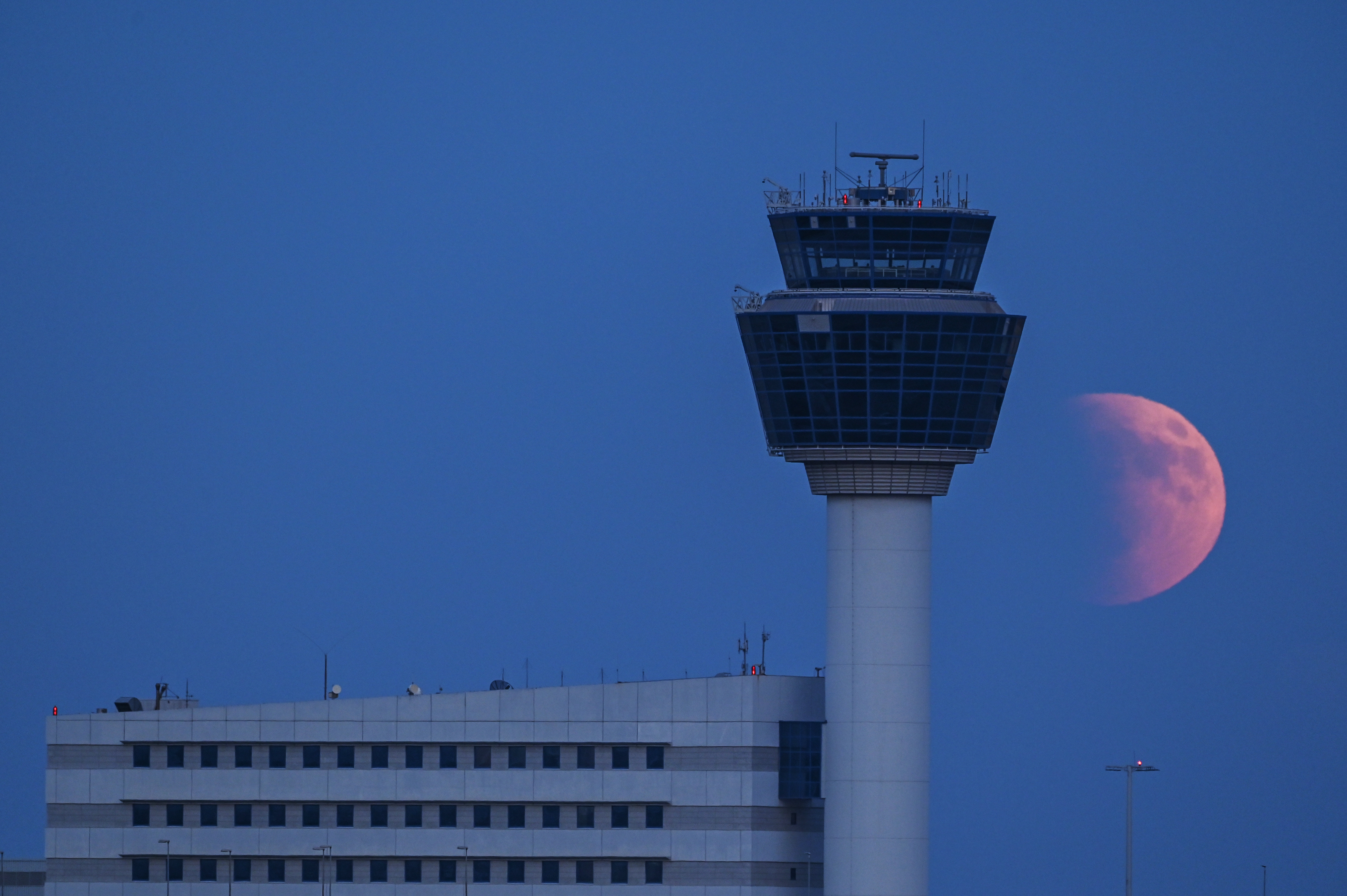 A photograph of the &quot;blood moon&quot; beside an air traffic control tower at Athens Airport in Greece.