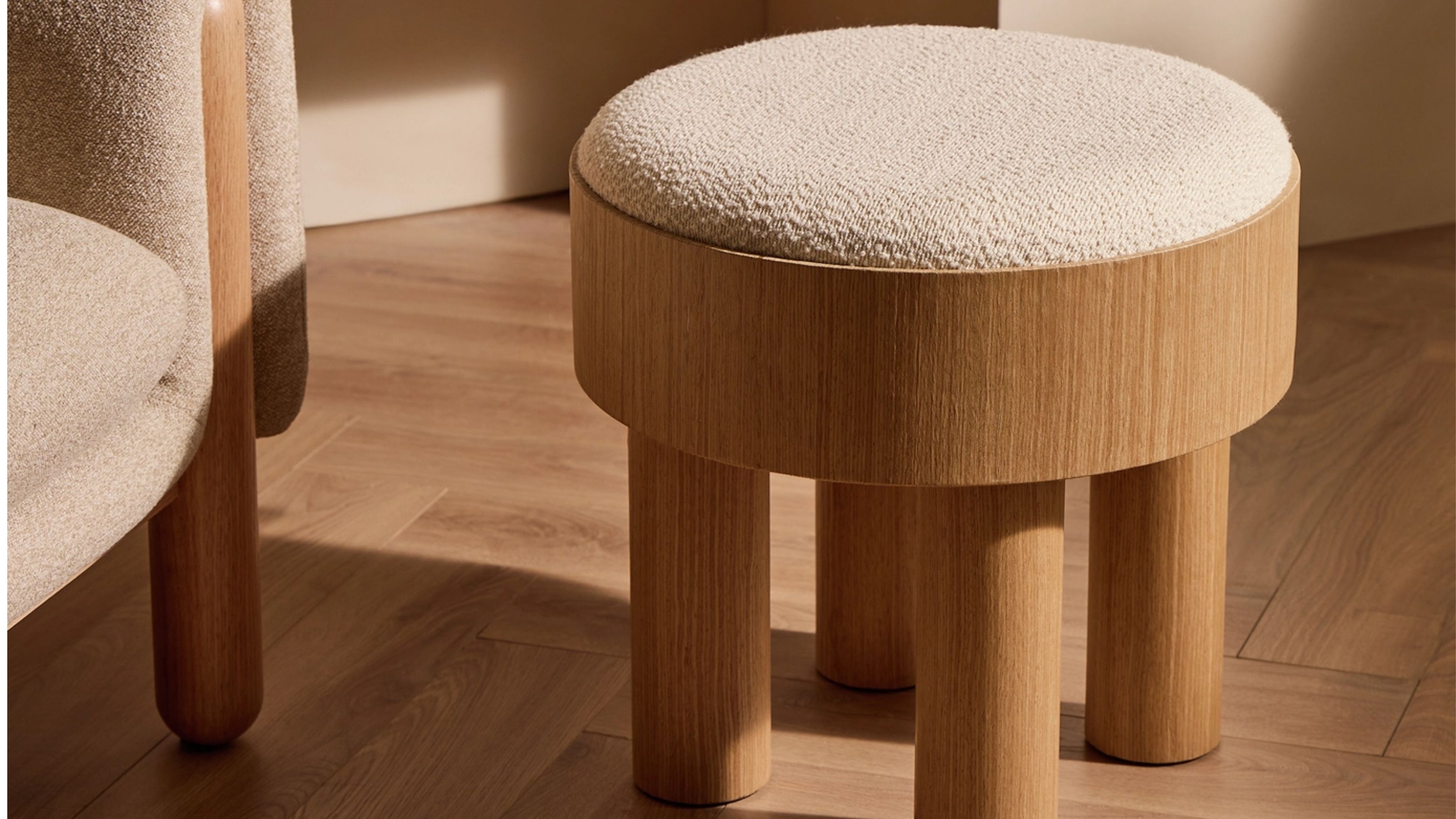 Close-up image of a wooden footstool with a white boucle upholstery top.