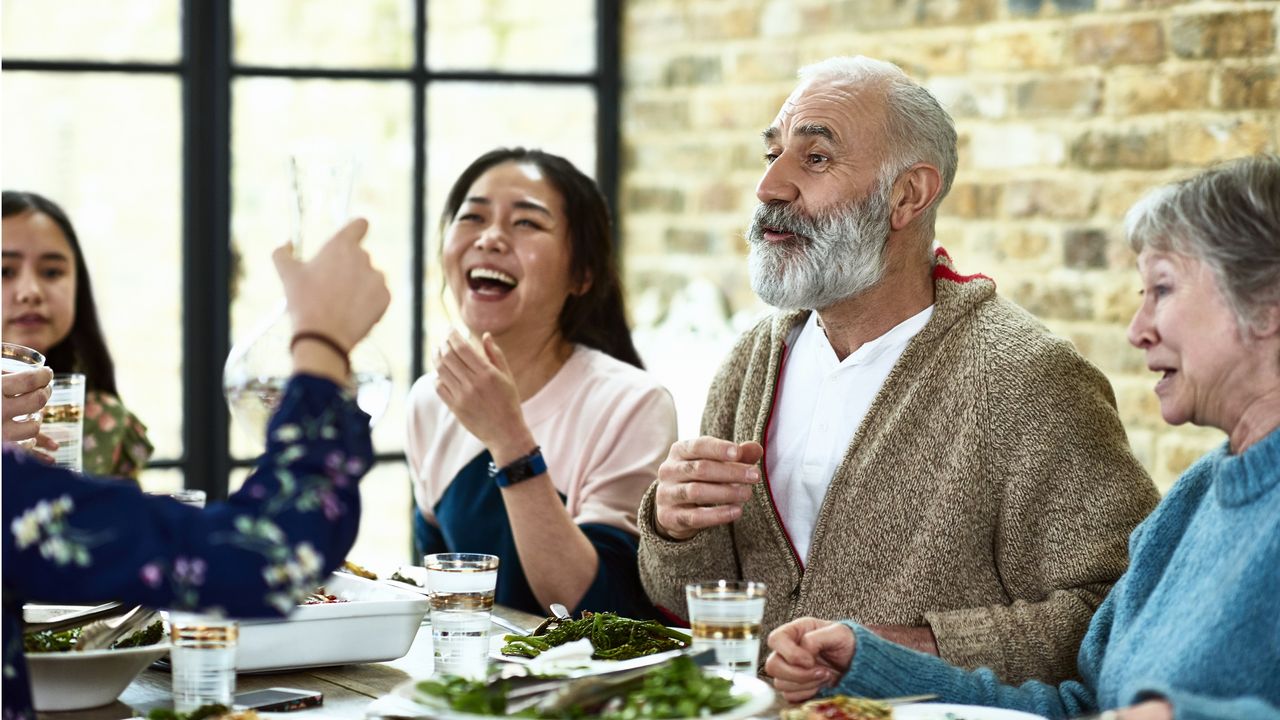 An older couple laughs with family during a meal.