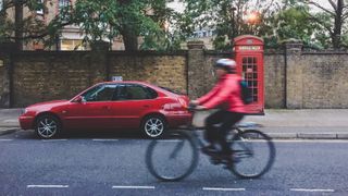 A cyclist riding next to a parked car and a telephone box