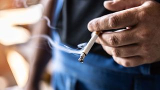 A close up of a man's hand holding a lit cigarette that's smoking