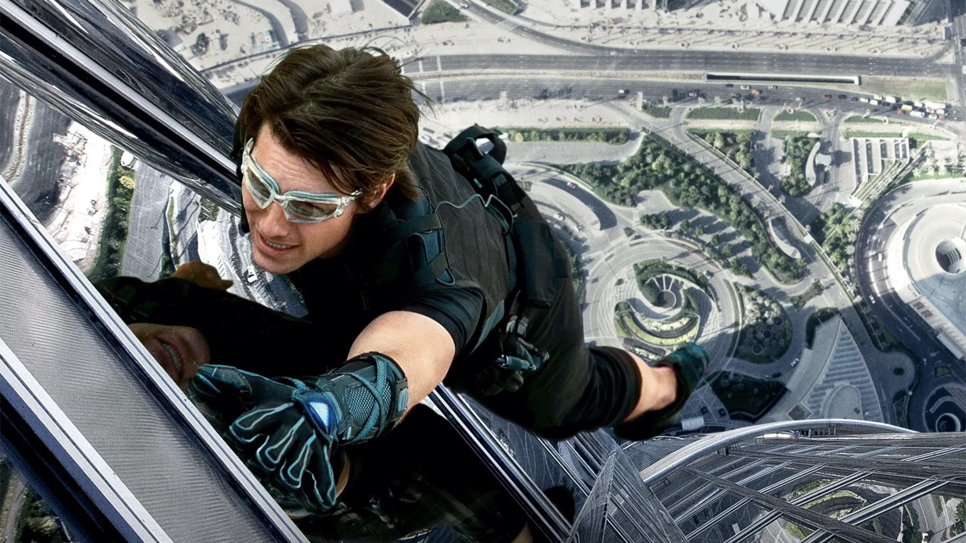 Mission Impossible movies in order: Tom Cruise as Ethan Hunt climbing a tall building during Mission Impossible Ghost Protocol.