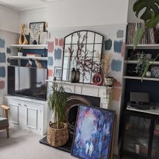 Fireplace in a white living room with built-in alcove unit, showing paint samples on the chimney breast around a framed mirror