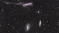 A trio of galaxies are pictured shining in deep space against a starfield dotted with more distant galaxies.