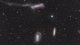A trio of galaxies are pictured shining in deep space against a starfield dotted with more distant galaxies.