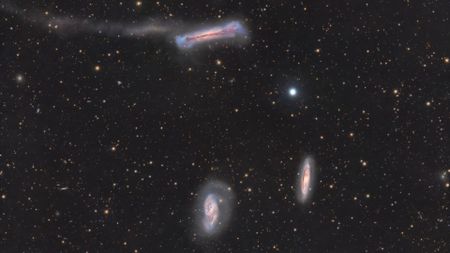 A trio of galaxies are pictured shining in deep space against a starfield dotted with more distant galaxies.