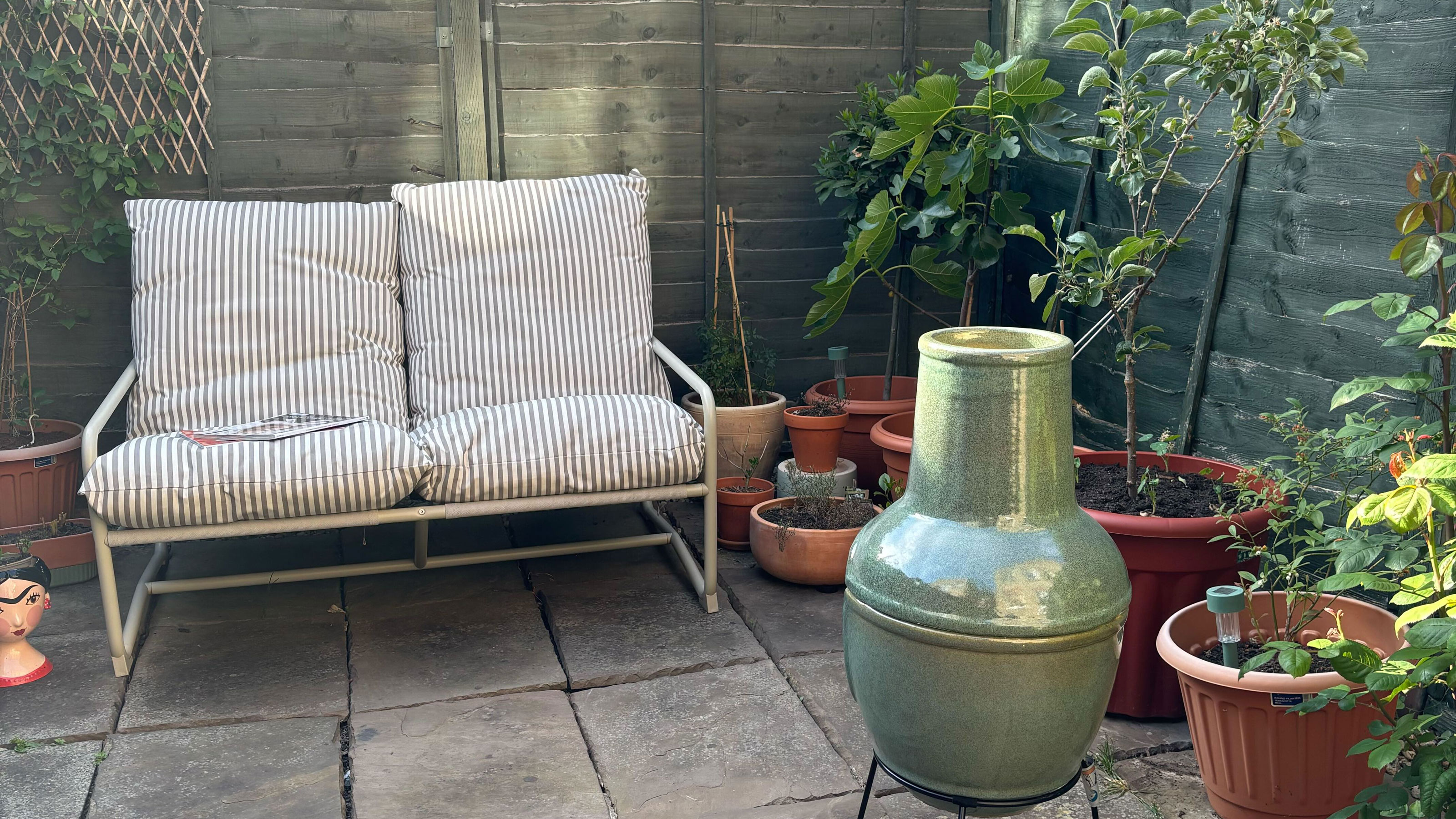 Green chiminea in a patio courtyard garden with a striped sofa