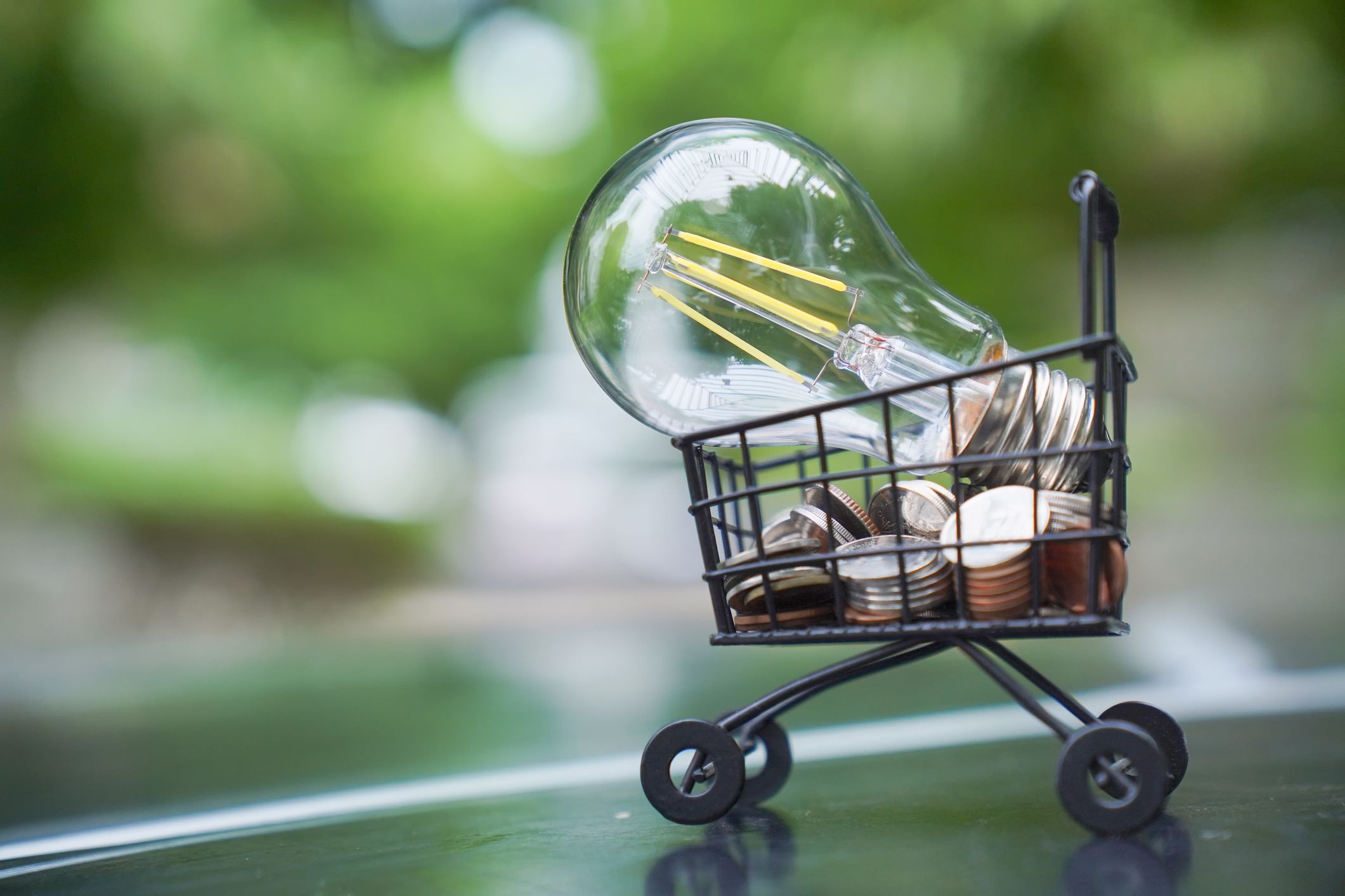 a light bulb sitting on top a stack of coins in a shopping cart indicating energy savings