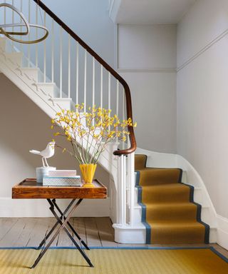Colorful hallway with yellow stair runner and rug, wooden console table with yellow flowers, books and ornaments, white painted walls, wooden flooring, contemporary rounded light fixture