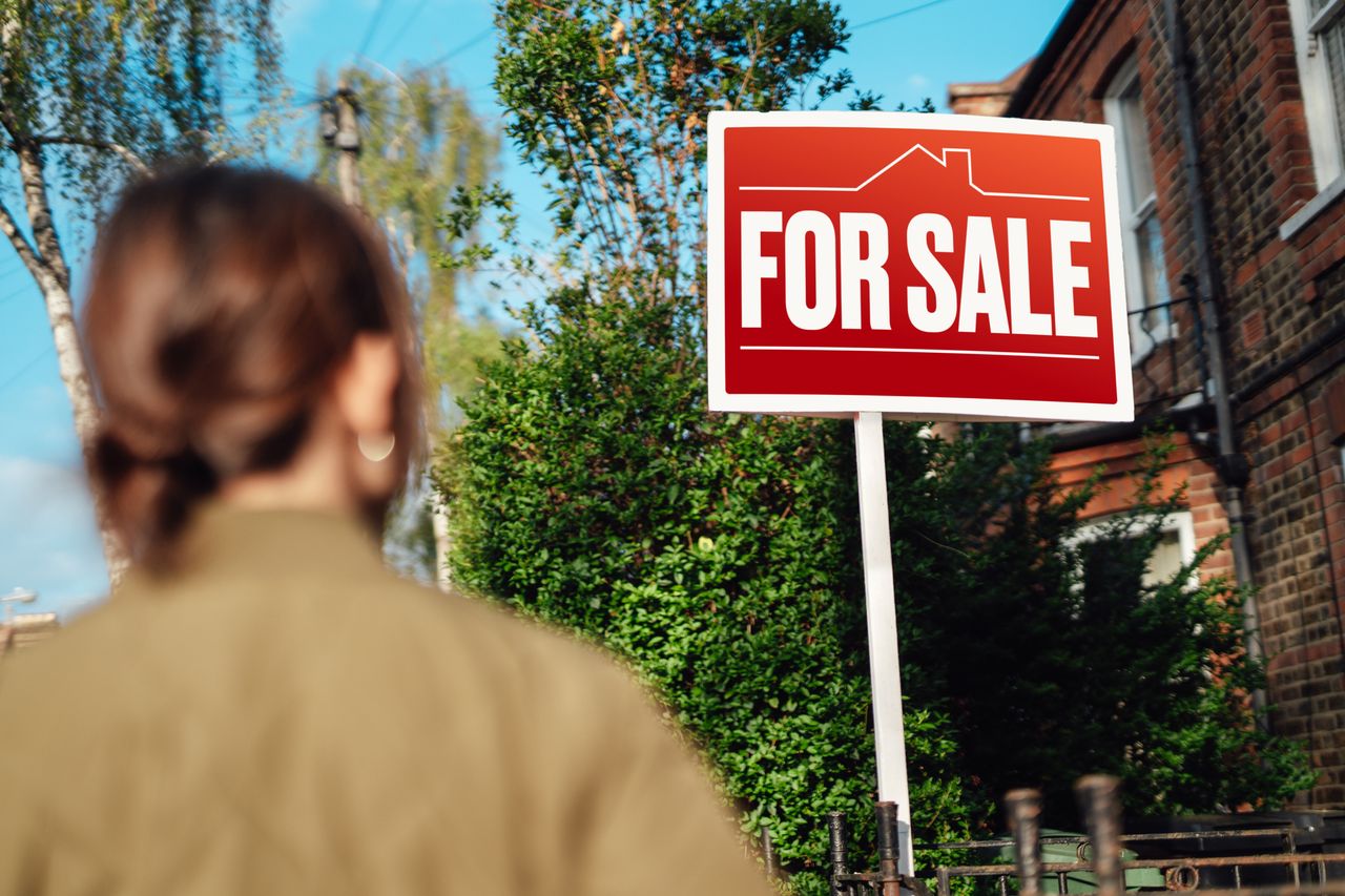 Rear view of woman looking looking at real estate sign, planning to buy a home.