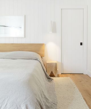 neutral shiplapped white bedroom with a wooden bedframe and headboard, small wooden side table, seaside photography wall art and gray linen bedding