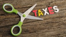 Scissors poised to cut into the word "taxes" on a wooden background.