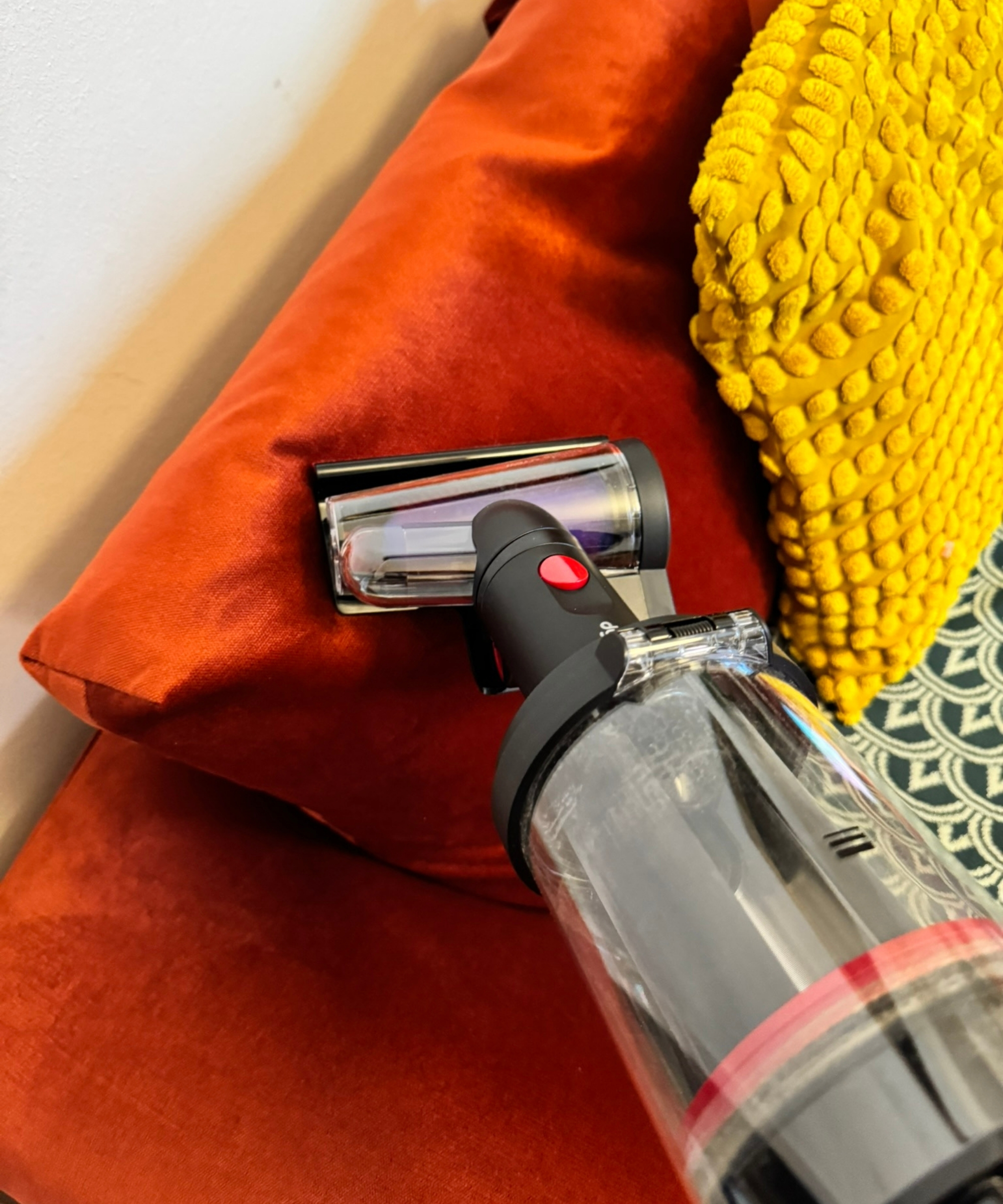 Dyson V16 Piston Animal vacuuming orange sofa in handheld mode, using Dyson hair screw tool.
