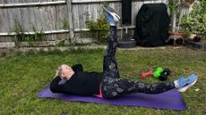 Kat Storr doing Pilates scissors exercise on yoga mat in garden