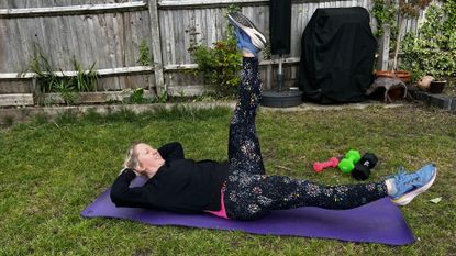 Kat Storr doing Pilates scissors exercise on yoga mat in garden
