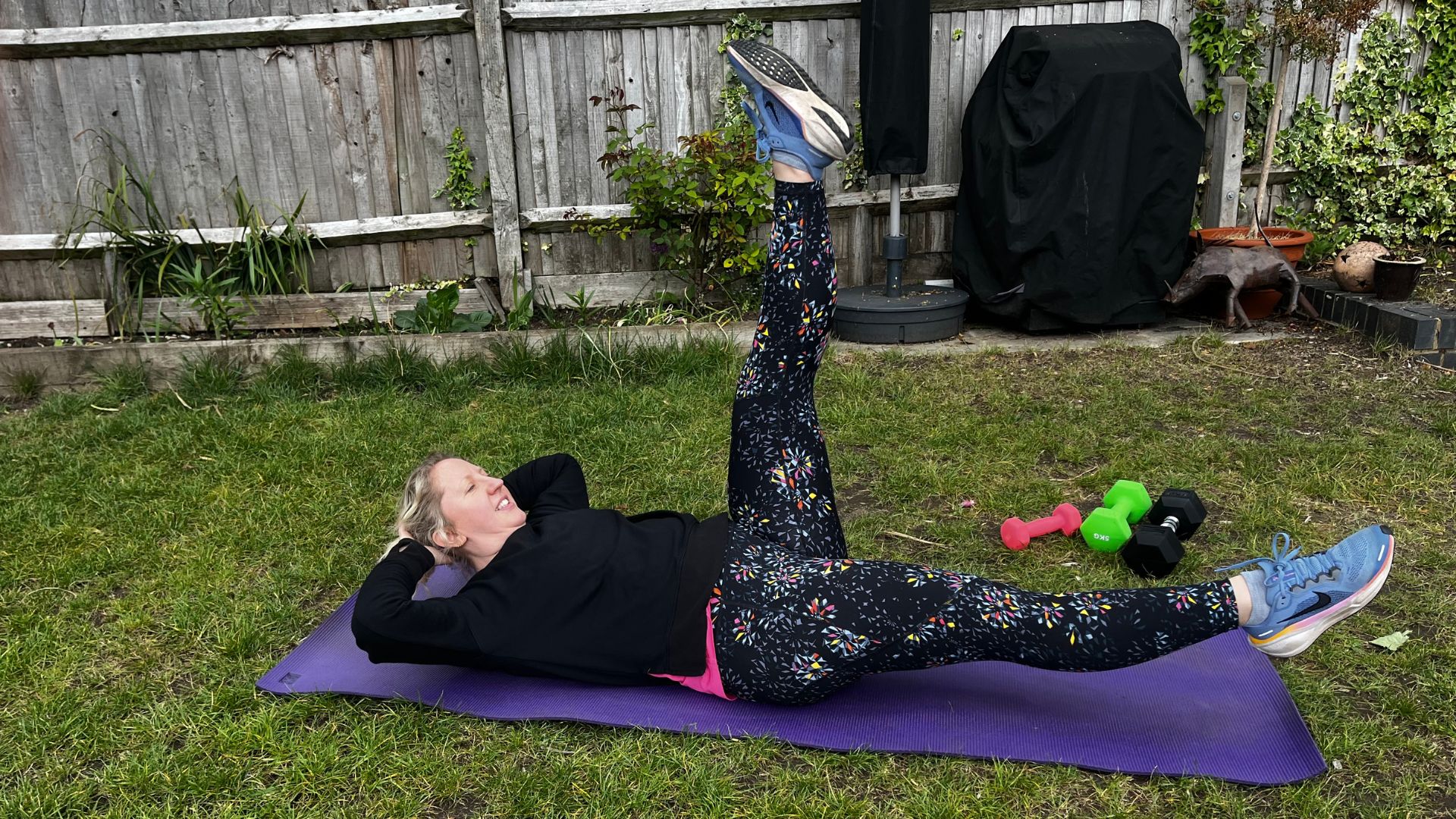 Kat Storr doing Pilates scissors exercise on yoga mat in garden