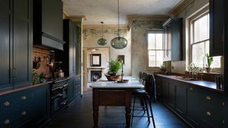 large dark blue kitchen in period property with copper splashback, large island with seating, window above sink, dark wooden floor, pendant lighting above island