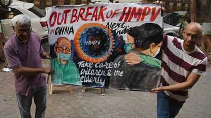 Two people holding poster warning of HMPV