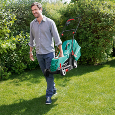 man in blue jeans carrying lawnmower on green grass
