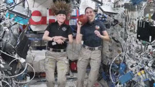 An astronaut throws a football on a clutter space station while another smiles to her side.